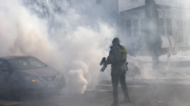 Seorang agen federal berpatroli di lokasi insiden penembakan Alex Pretti di Minneapolis, Minnesota. Foto menunjukkan penggunaan senjata anti-huru-hara dan kepulan asap selama operasi penegakan imigrasi.