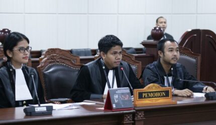 "Tim pemohon FAIN mengenakan jas hitam dan jubah pengacara saat mengikuti sidang uji materiil UU ASN di Mahkamah Konstitusi, duduk di belakang meja dengan tanda 'Pemohon'."