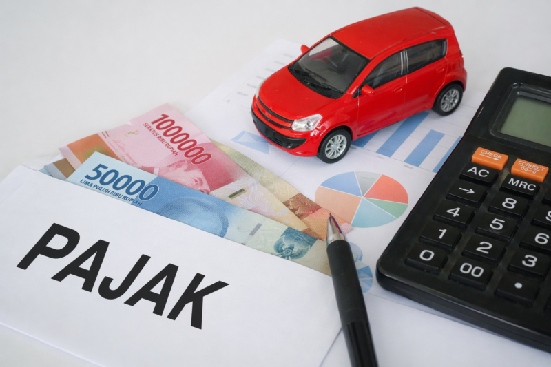 Ilustrasi perhitungan pajak kendaraan listrik di Indonesia, menampilkan kalkulator, uang rupiah, dokumen grafik, dan miniatur mobil sebagai gambaran biaya kepemilikan BYD Atto 1 jika insentif pajak berubah.