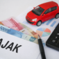 Ilustrasi perhitungan pajak kendaraan listrik di Indonesia, menampilkan kalkulator, uang rupiah, dokumen grafik, dan miniatur mobil sebagai gambaran biaya kepemilikan BYD Atto 1 jika insentif pajak berubah.