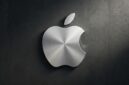 Logo Apple berbahan logam perak dengan tekstur melingkar yang elegan, terpasang pada dinding beton gelap.(poto: AI).