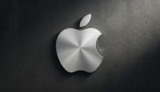 Logo Apple berbahan logam perak dengan tekstur melingkar yang elegan, terpasang pada dinding beton gelap.(poto: AI).