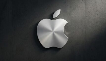 Logo Apple ikonik bertekstur logam perak (brushed metal) dengan guratan melingkar, terpasang kokoh di tengah dinding beton gelap yang bertekstur kasar dengan pencahayaan dramatis dari samping.