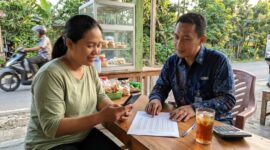 Petugas Mantri BRI menjelaskan tabel simulasi angsuran KUR kepada pelaku usaha mikro di warung kelontong.(ilustrasi poto: AI).